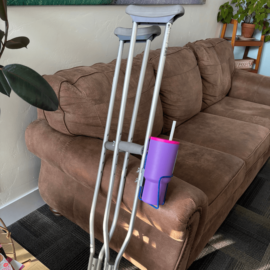 Translation missing: en.Crutch Drink Holder attached to crutches on a couch, showcasing its aluminum design for easy access to beverages