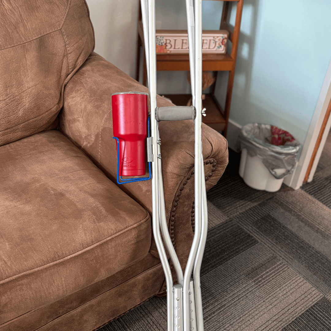 Translation missing: en.Crutch Drink Holder attached to crutches in a living room setting, holding a red cup for easy access